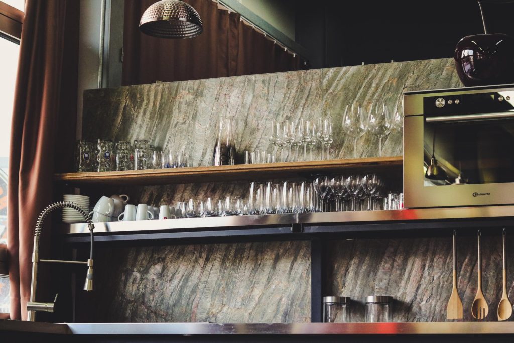 Kitchen with cream quartz countertop, sink, stove, pendant lighting, and glass crockery shelf